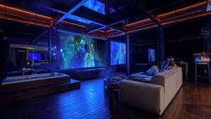A modern interior with a wooden floor, a sofa, a coffee table, and a large screen displaying a movie. - KClub Ubud (Tegallalang)