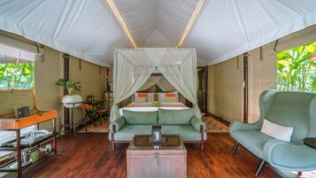 A tented room with a bed, green sofa, and a table with a lamp.