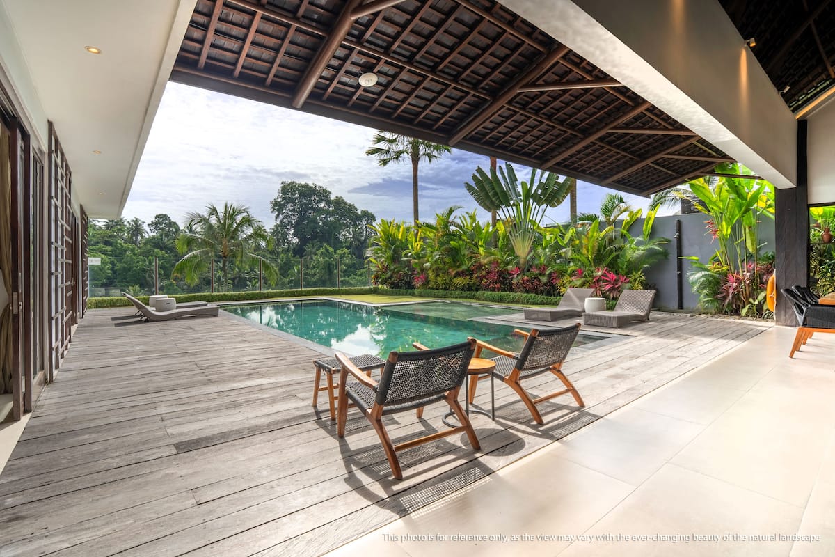 A wooden deck with a pool, lounge chairs, and tropical plants.