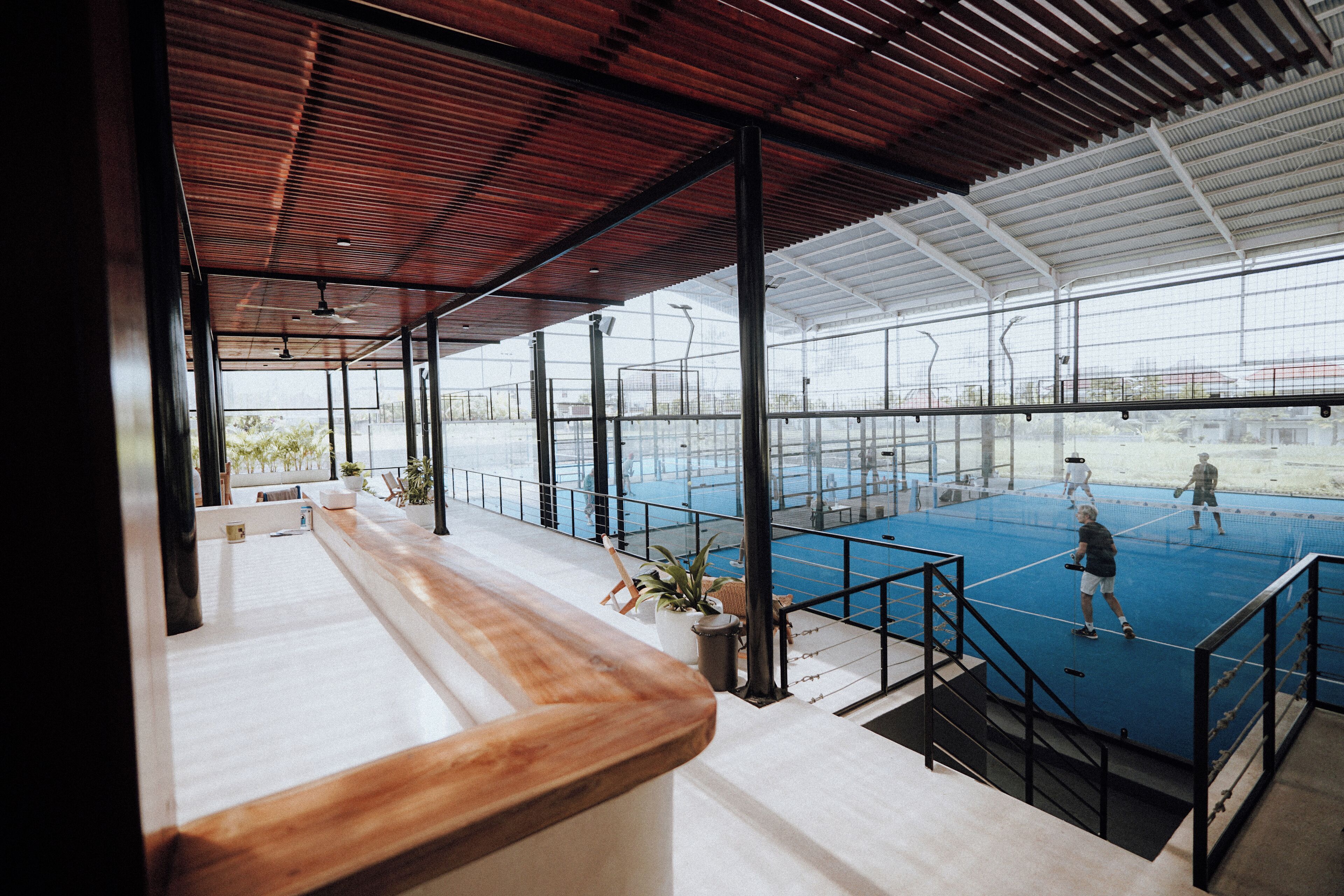 A tennis court with a net, surrounded by glass walls and a wooden ceiling.