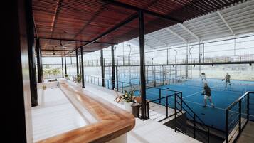A tennis court with a net, surrounded by glass walls and a wooden ceiling.