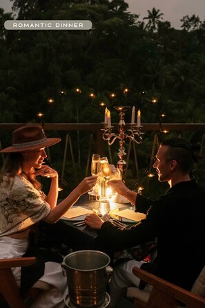 A couple dining outdoors at night with string lights and candles, surrounded by trees. - KClub Ubud (Tegallalang)
