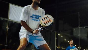 Jugador de tenis con camisa y pantalones cortos en una cancha cubierta, sosteniendo una raqueta.