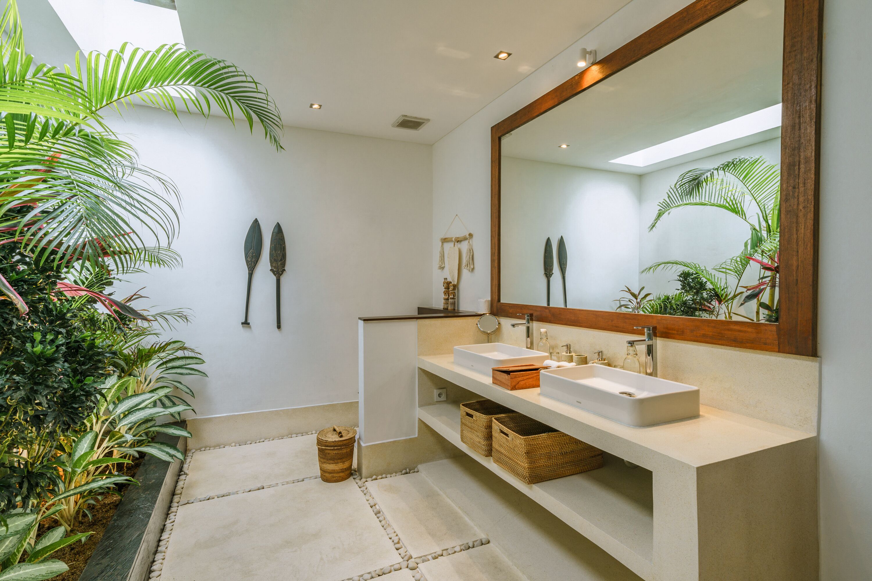 Un baño moderno con dos lavamanos, un espejo grande y una pequeña zona con plantas.