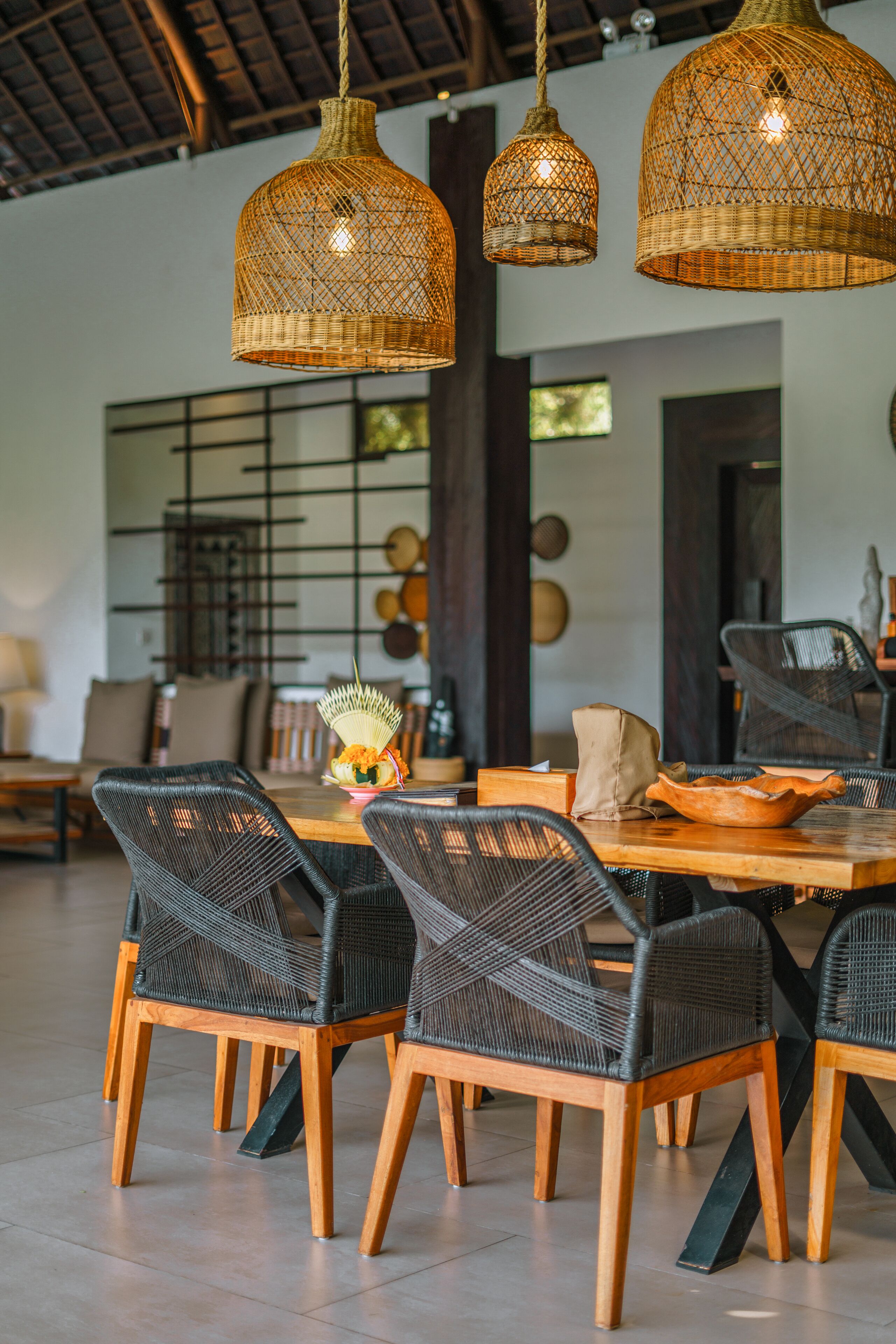 Un comedor con sillas de mimbre, una mesa de madera y lámparas colgantes de mimbre.