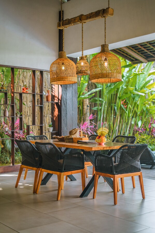 A dining area with a wooden table and black wicker chairs, surrounded by lush greenery and bamboo walls. - KClub Ubud (Tegallalang)