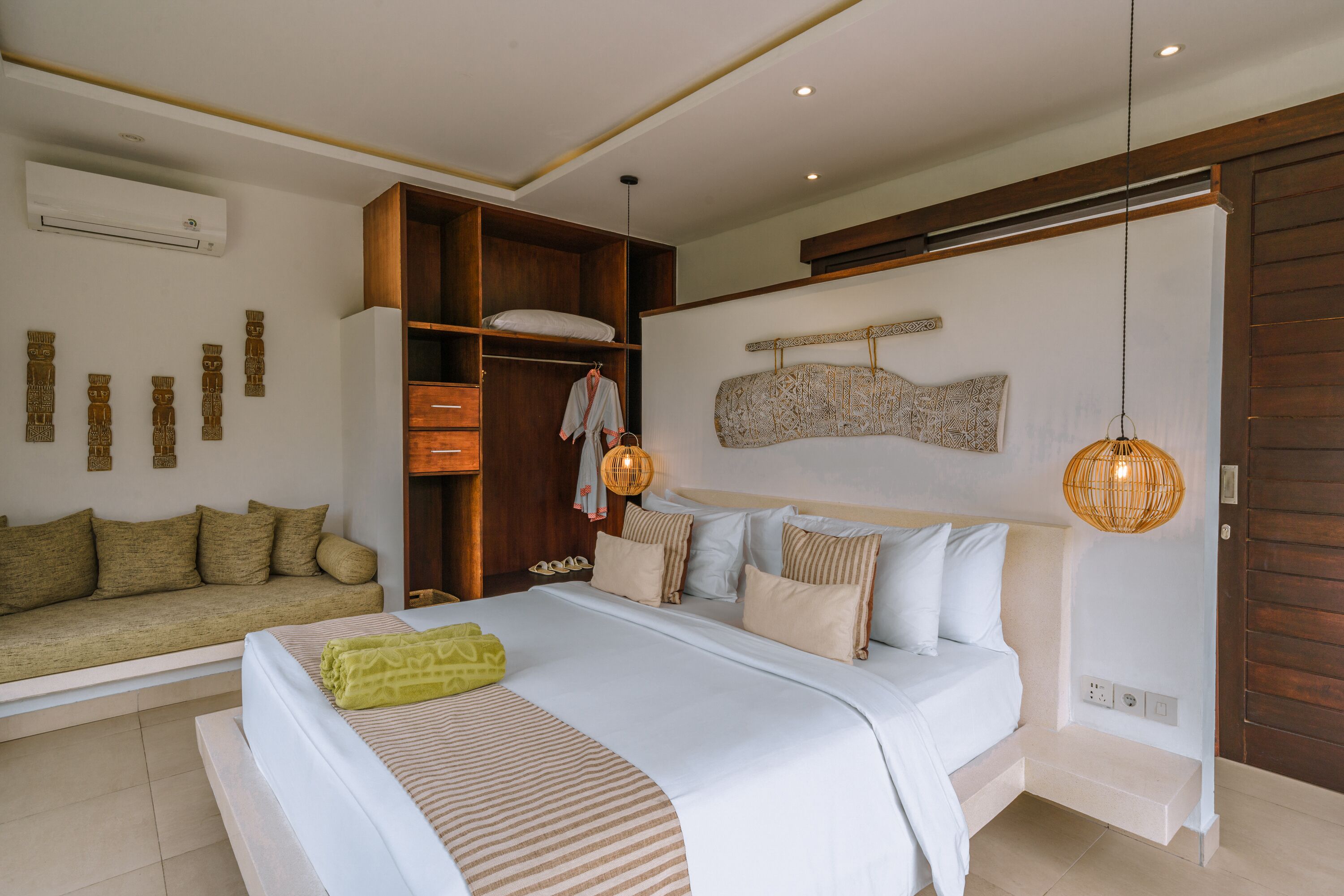 A bedroom with a large bed, a wooden wardrobe, a sofa, and a wall-mounted shelf.
