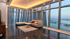 A modern living room with a large window, a sofa, a coffee table, and a decorative floor lamp. - WATERFRONT HOTEL  APARTMENT (Lusail)