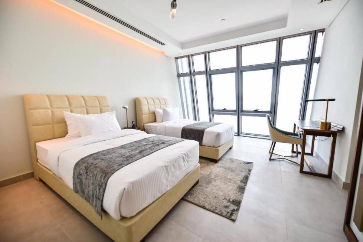 A modern bedroom with two beds, a desk, and large windows.