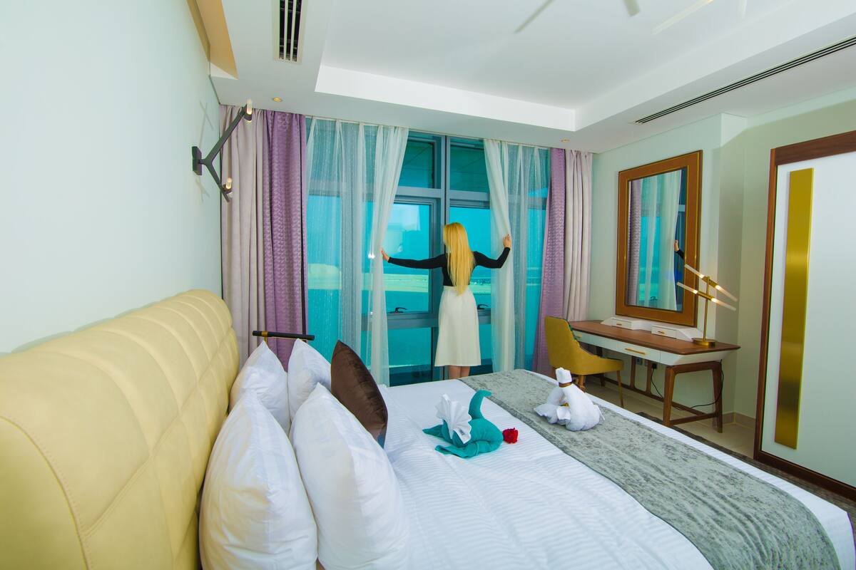 A hotel room with a bed, a desk, a chair, and a large window with curtains.