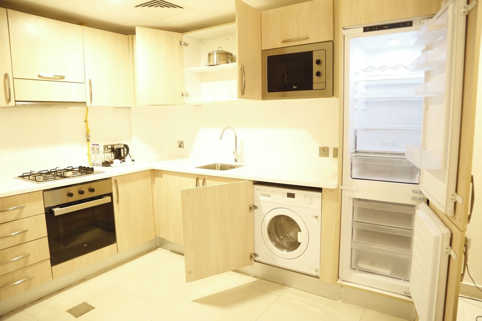 Een kleine keuken met een gasfornuis, oven, magnetron, spoelbak en een inbouw wasmachine.