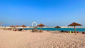 A beach with thatched umbrellas, sun loungers, and a clear blue sky. - WATERFRONT HOTEL  APARTMENT (Lusail)