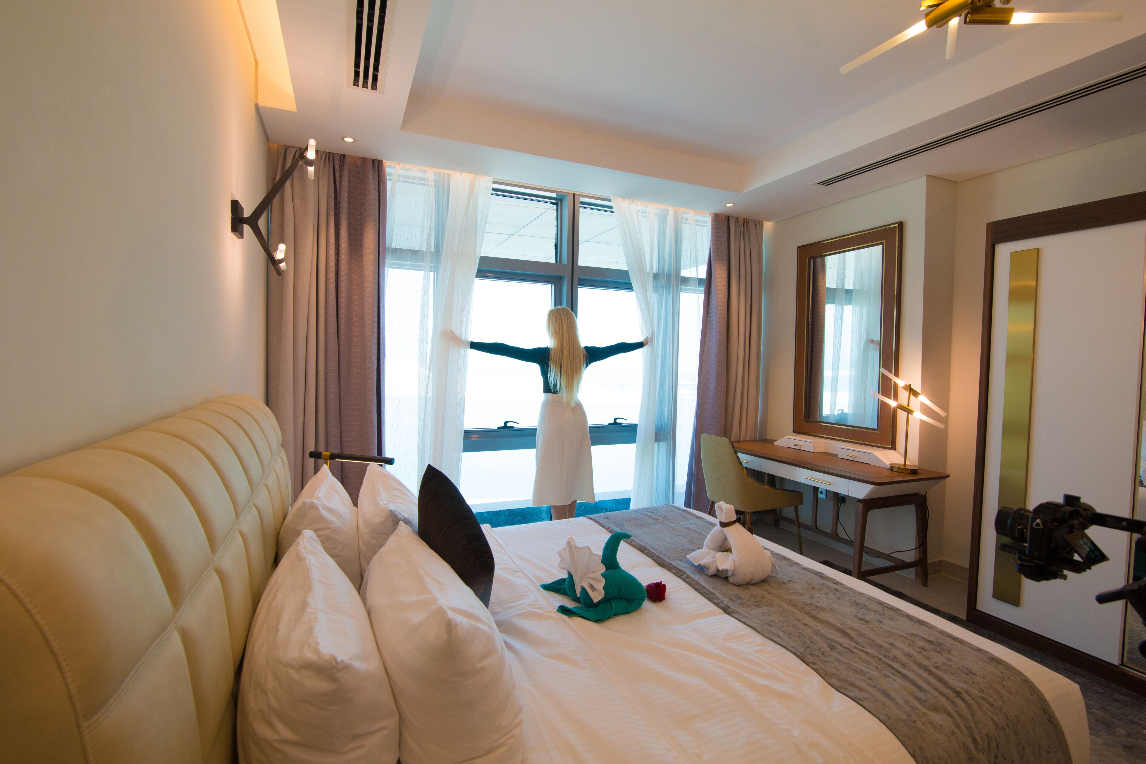 A hotel room with a bed, a desk, a chair, a mirror, and a window with curtains.