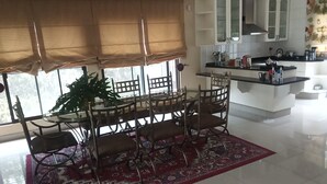 Une cuisine moderne avec des meubles blancs, un coin repas agrémenté d’un tapis à motifs rouges et une grande fenêtre avec des stores.