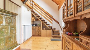 A wooden staircase leading to a second floor, a kitchen area with wooden cabinets and a radiator, and a wooden dining table with a vase. - Holiday House Podhamer Boris With Private Wellness (Ljutomer)