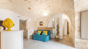 A cozy room with a stone wall, a blue sofa with yellow and blue cushions, and a wooden headboard. - Trullo Aia Antica - Ceglie Messa... (Ceglie Messapica)