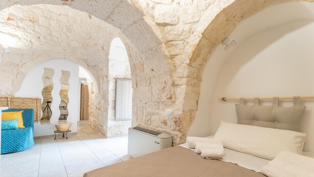 A bedroom with a large bed, a blue chair, and a stone wall. - Trullo Aia Antica - Ceglie Messa... (Ceglie Messapica)