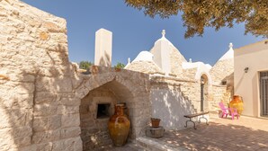A stone archway leading to a courtyard with a large vase, a bench, and a potted plant. - Trullo Aia Antica - Ceglie Messa... (Ceglie Messapica)