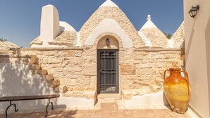 A stone building with a tiled roof, a door with a metal gate, and a large vase. - Trullo Aia Antica - Ceglie Messa... (Ceglie Messapica)
