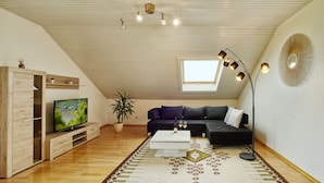 Een modern loft appartement met een schuine kap, een grote televisie, een zwarte bank, een salontafel en een dakraam.
