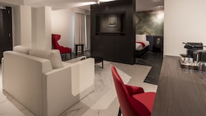 Una habitación de hotel moderna con sofá, sillones rojos, cama, televisor y cafetera.