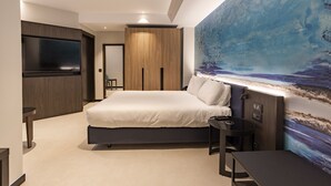 Un dormitorio moderno con una cama grande, un televisor montado en la pared y un cuadro de un paisaje marino.