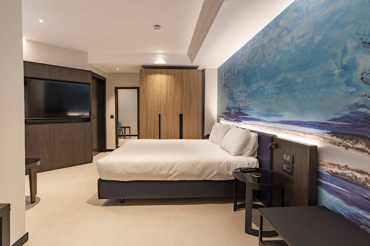 A modern bedroom with a large bed, a TV mounted on the wall, and a painting of a seascape.