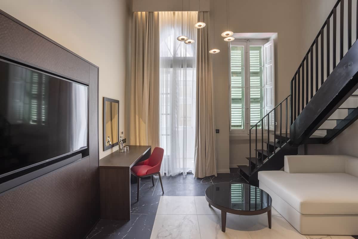 A modern living room with a flat-screen TV, a red chair, a glass coffee table, a sofa, and a staircase.