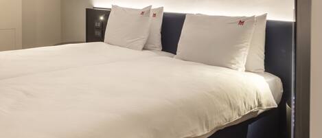 A neatly made bed with white bedding and pillows, a dark headboard, and a bedside table with a lamp.