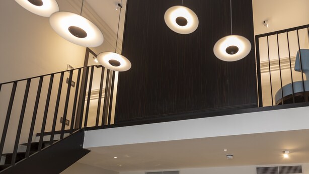 Un interior moderno con una escalera, una pared de madera oscura y varios apliques de luz circulares.