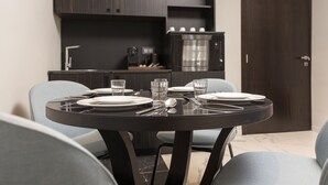 Un comedor con una mesa redonda dispuesta para cuatro personas, con platos, vasos, cubiertos y una cafetera.