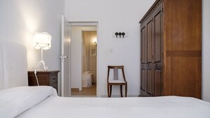 Un dormitorio con cama, mesita de noche, silla, armario y puerta que da al baño.