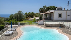 Una piscina con vistas despejadas al mar, rodeada por un edificio blanco con un patio y un pequeño jardín.