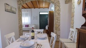 Un comedor con un arco de piedra, sillas blancas, una mesa preparada para cuatro personas y una botella de vino.