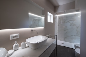A modern bathroom with a large oval sink, a mirror, a shower with glass doors, and a toilet. - Cozzo Tirone (Avola)