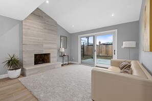 Una sala de estar moderna con chimenea, un sofá y un amplio ventanal corredera que da a un espacio exterior.