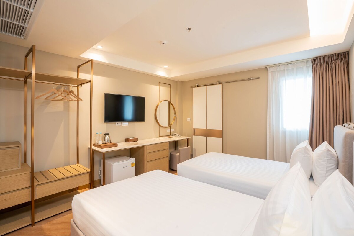 A hotel room with two beds, a desk with a flat-screen TV, a mirror, and a wardrobe.