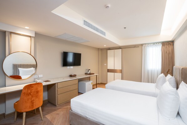 A hotel room with a desk, two beds, a TV, a mirror, and a wardrobe.