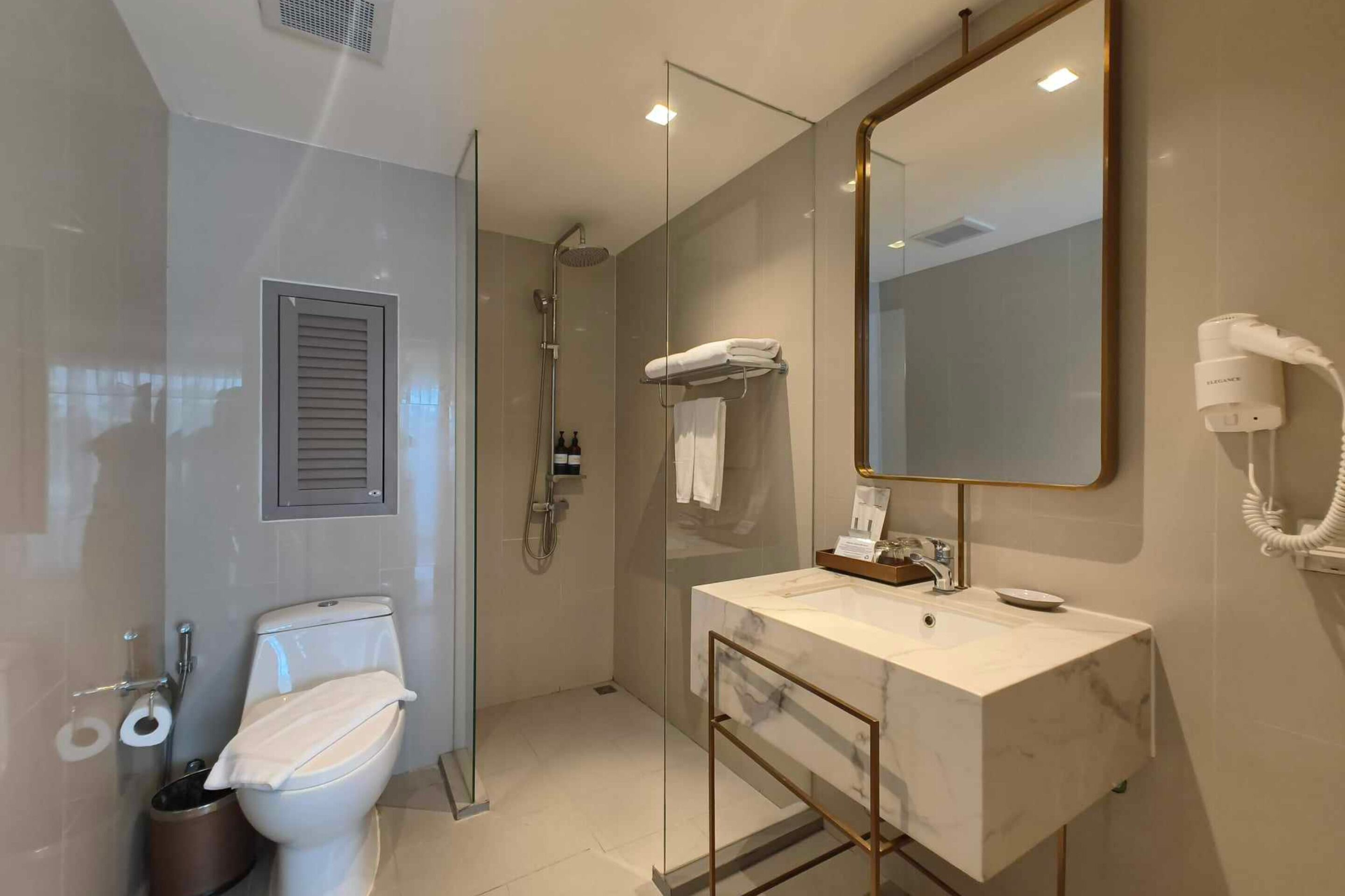A modern bathroom with a glass-enclosed shower, a white toilet, a marble sink, and a large mirror.