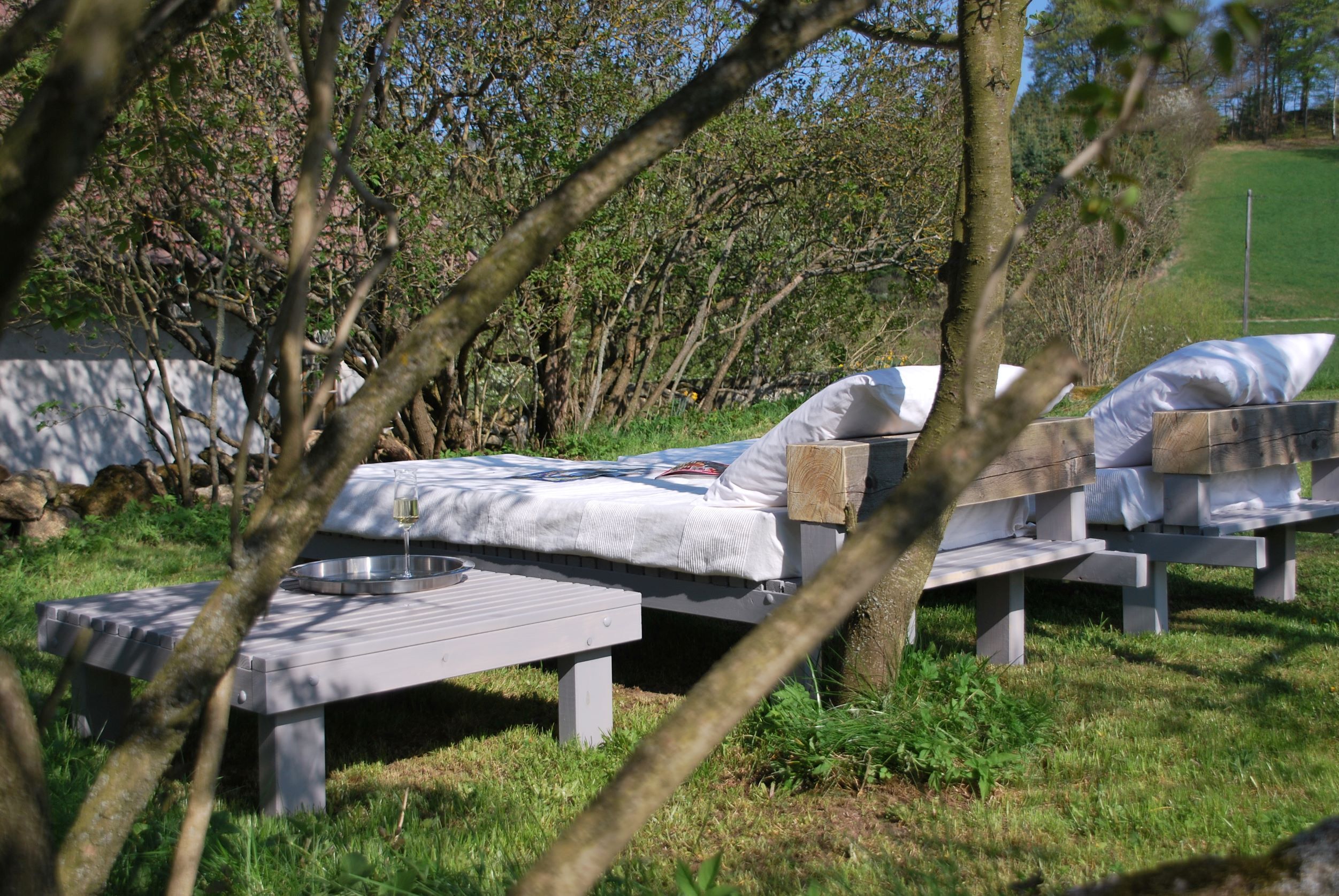 Un espace extérieur paisible, aménagé avec deux bancs en bois, chacun agrémenté d’un coussin blanc et d’une petite table.