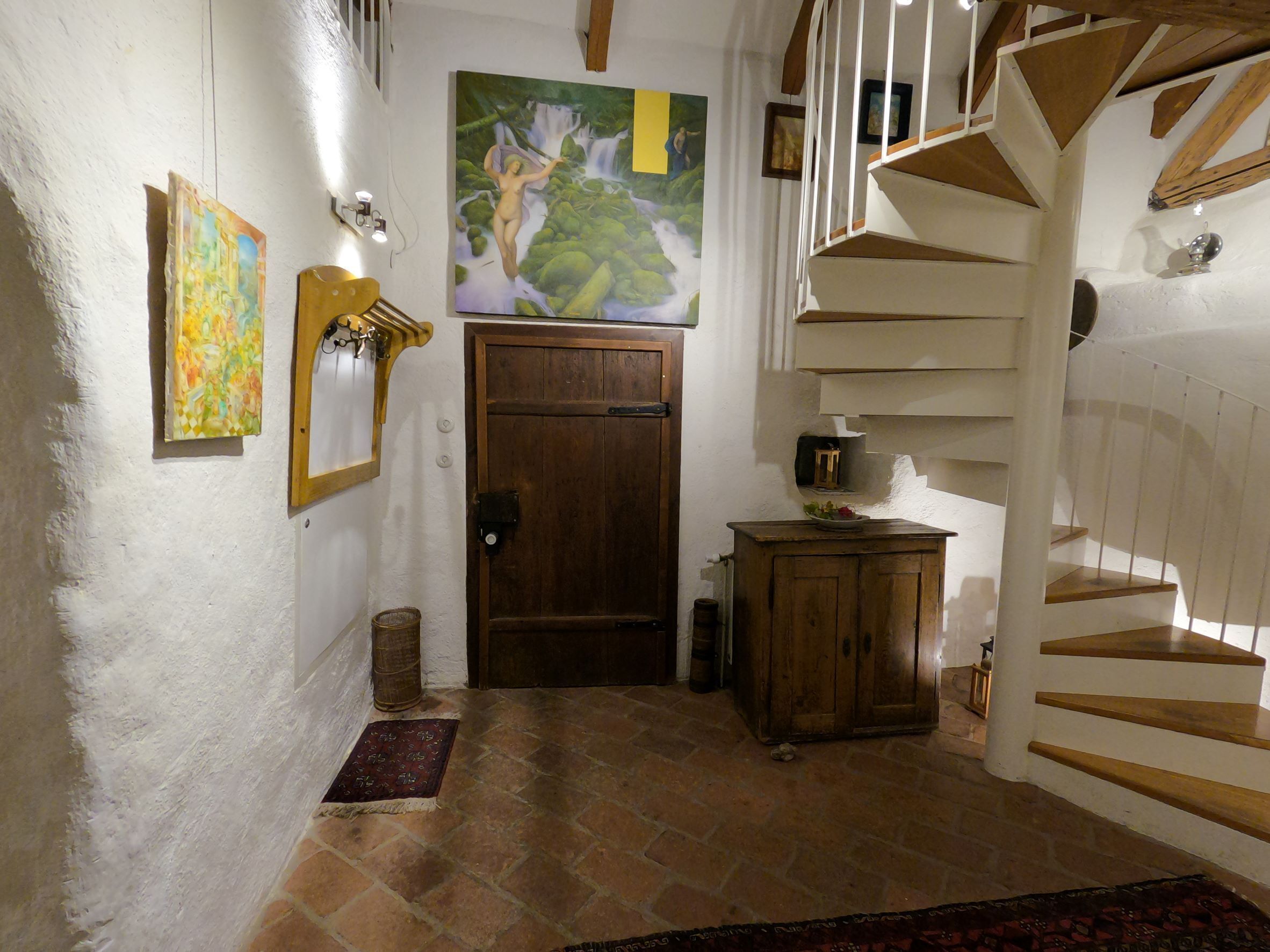 A staircase leading to a second floor, a wooden door, a painting, and a small cabinet.