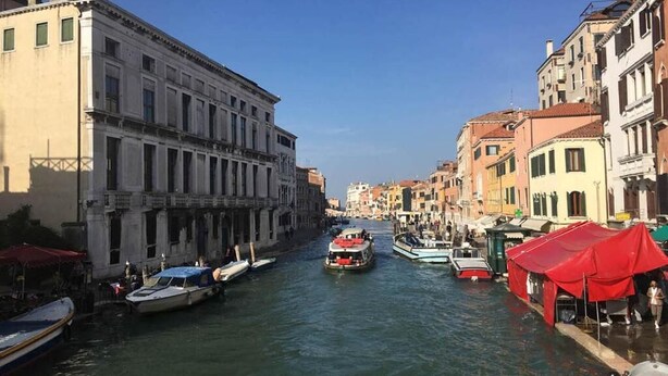 A canal with boats, historic buildings, and red canopies along the water's edge. - Ca' Berto Apartment (Venezia)