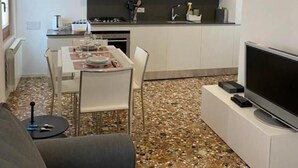 A compact living space with a dining area, kitchenette, and a flat-screen TV on a stand. - Ca' Berto Apartment (Venezia)