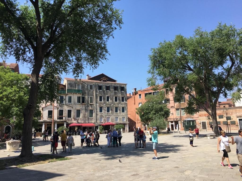 Una plaza pública con gente caminando, árboles y edificios históricos.
