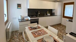 A compact kitchen with white cabinets, a countertop, and a dining area with a table set for two. - Ca' Berto Apartment (Venezia)