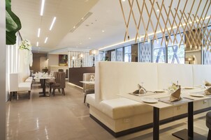 A modern restaurant with white booths, tables with set dining ware, and a ceiling with linear lighting.