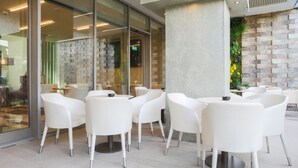 A modern indoor seating area with white chairs and tables, a glass wall, and a textured wall with a brick pattern. - The Legacy Luxury hotel Algiers Hydra (Algiers)