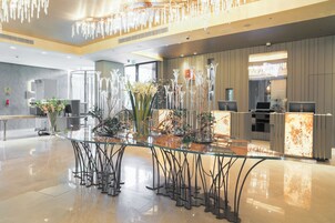 A modern hotel lobby with a glass-top reception desk, decorative vases, and a chandelier.