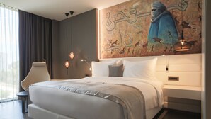 A modern bedroom with a large bed, a nightstand, a chair, and a wall mural. - The Legacy Luxury hotel Algiers Hydra (Algiers)