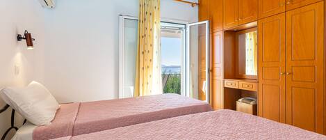 A bedroom with two beds, wooden cabinets, a ceiling fan, and a window with curtains.